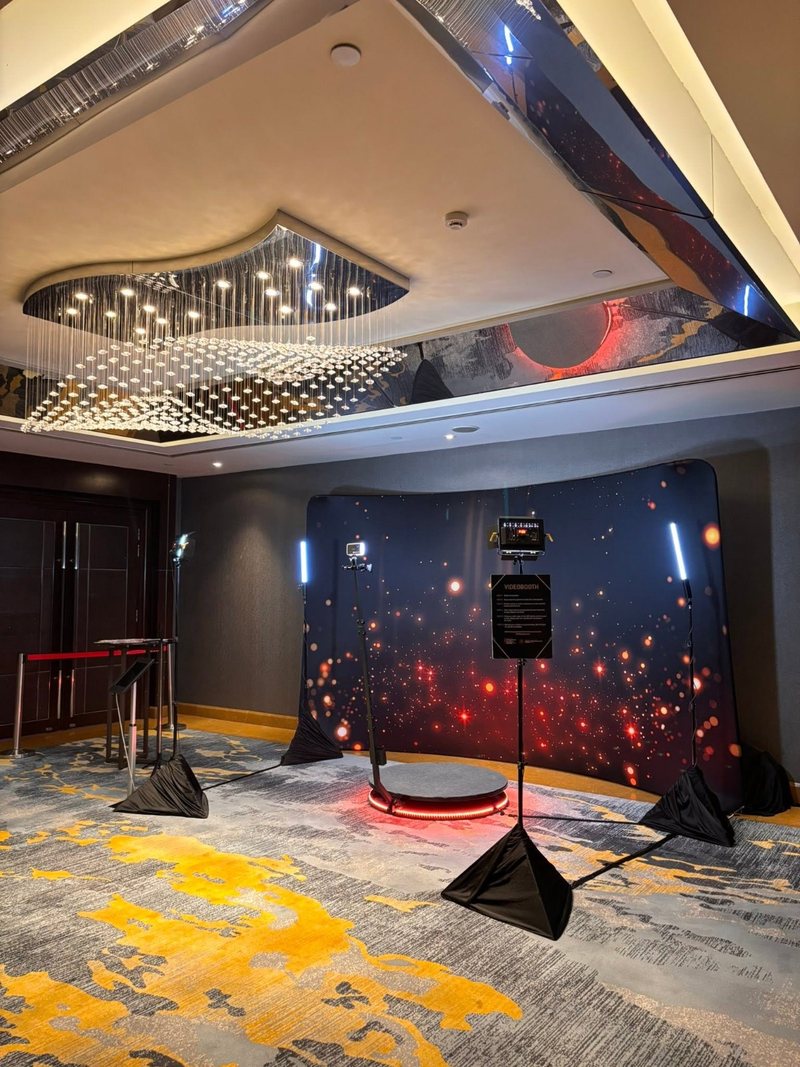 360 video booth platform with a red LED ring and rotating camera arm, set up against a curved backdrop in a hotel foyer